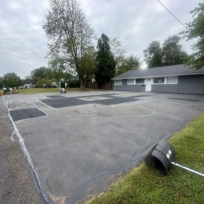 Asphalt lot with recently sealed areas. A building with a dark roof is on the right.