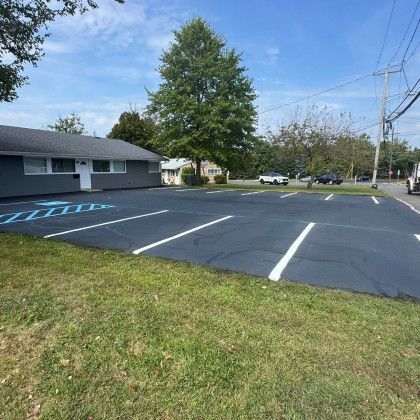Asphalt parking lot with painted white lines, next to a building and grass. Cars parked in the distance.