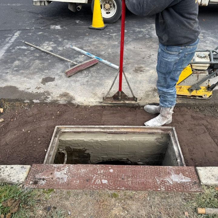 Person working on a manhole in a paved area, surrounded by tools and equipment.