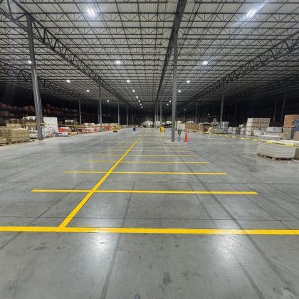 Empty warehouse interior with yellow painted lines on a concrete floor, and boxes are stacked along the sides.