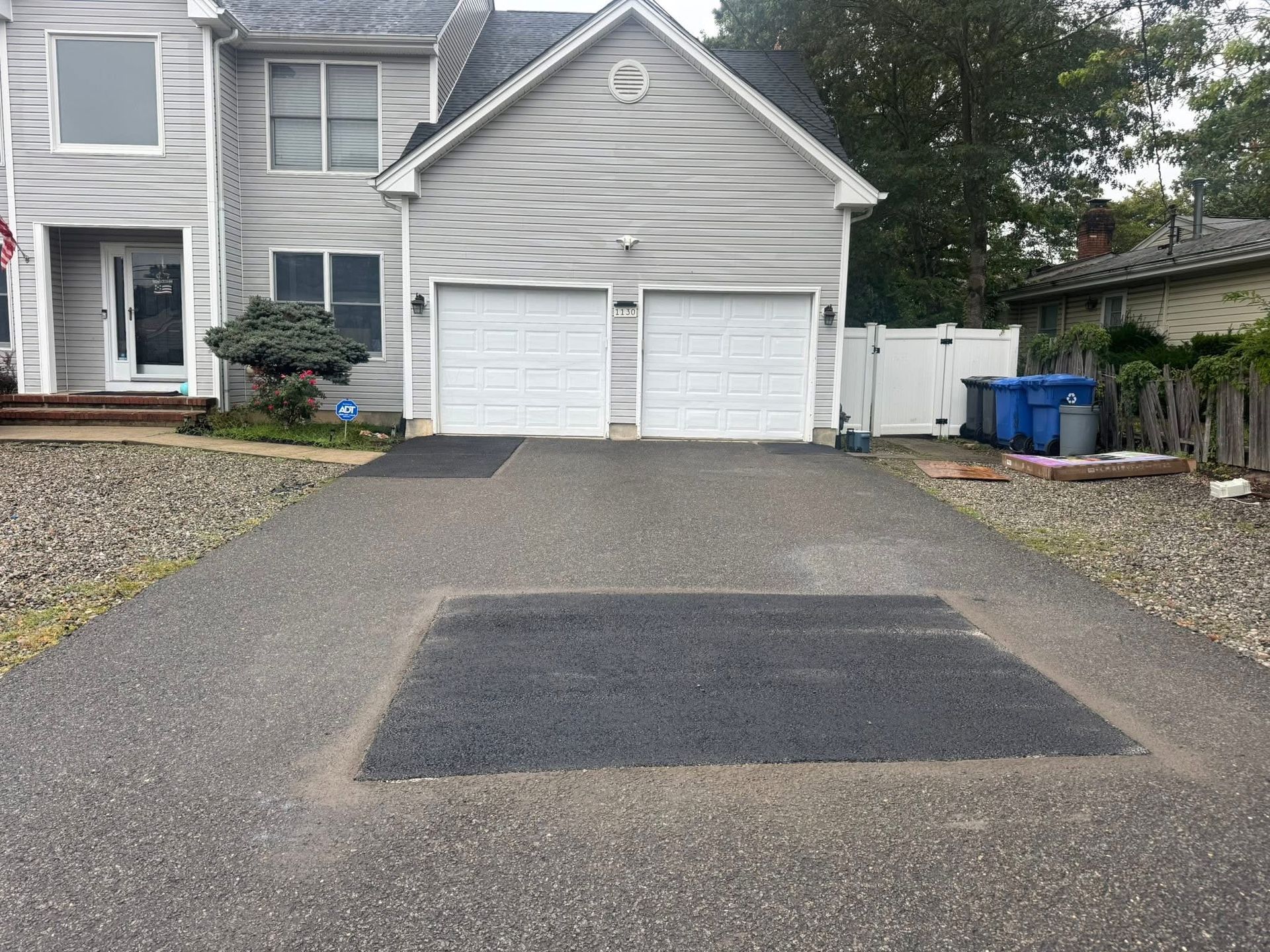 Gravel driveway leading to a two-car garage with a patched asphalt section in front