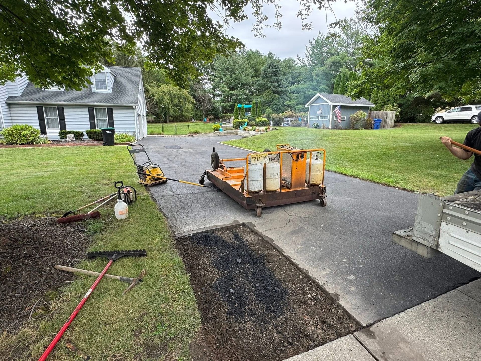 Driveway paving work with equipment and gravel beside a suburban house.