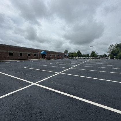 Empty black asphalt parking lot in front of a brick building under a cloudy sky.