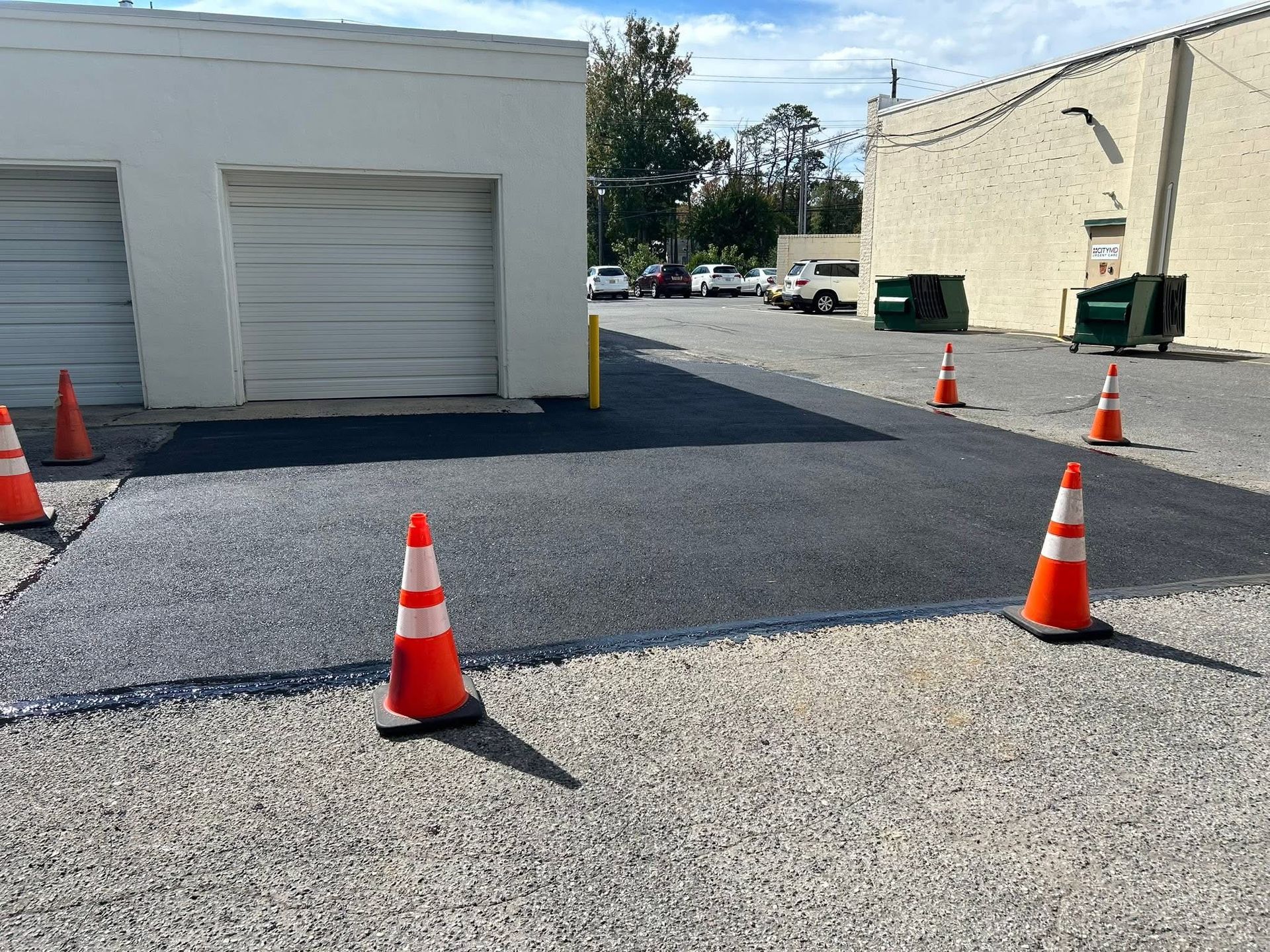 Orange traffic cones on a gravel lot between two white buildings on a sunny day