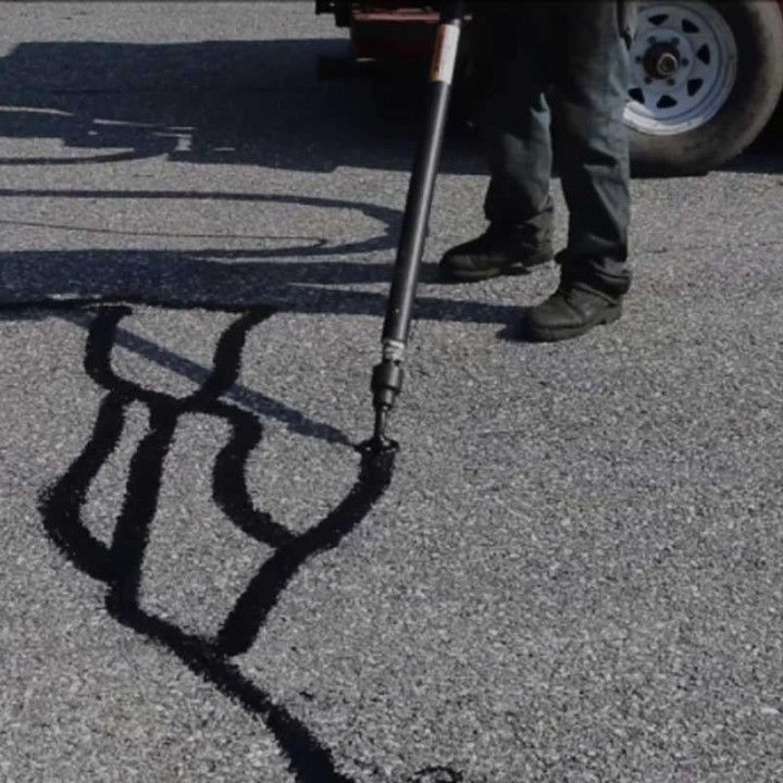 Person using a long-handled device to mark dark lines on pavement beside a parked vehicle