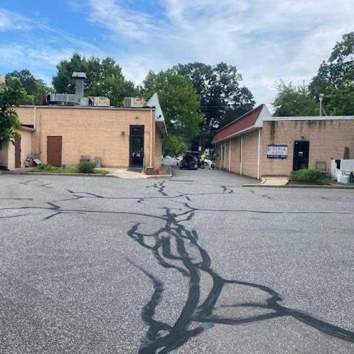 Parking lot with cracked asphalt between two tan buildings under a cloudy sky