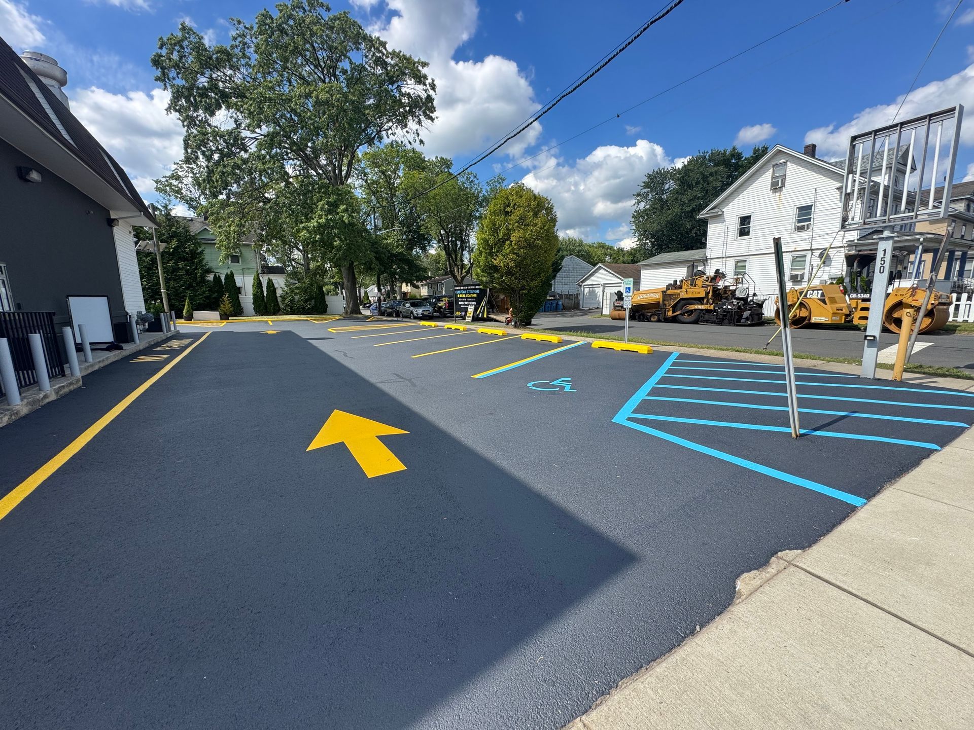 Newly paved parking lot with yellow and blue markings and a large yellow arrow.