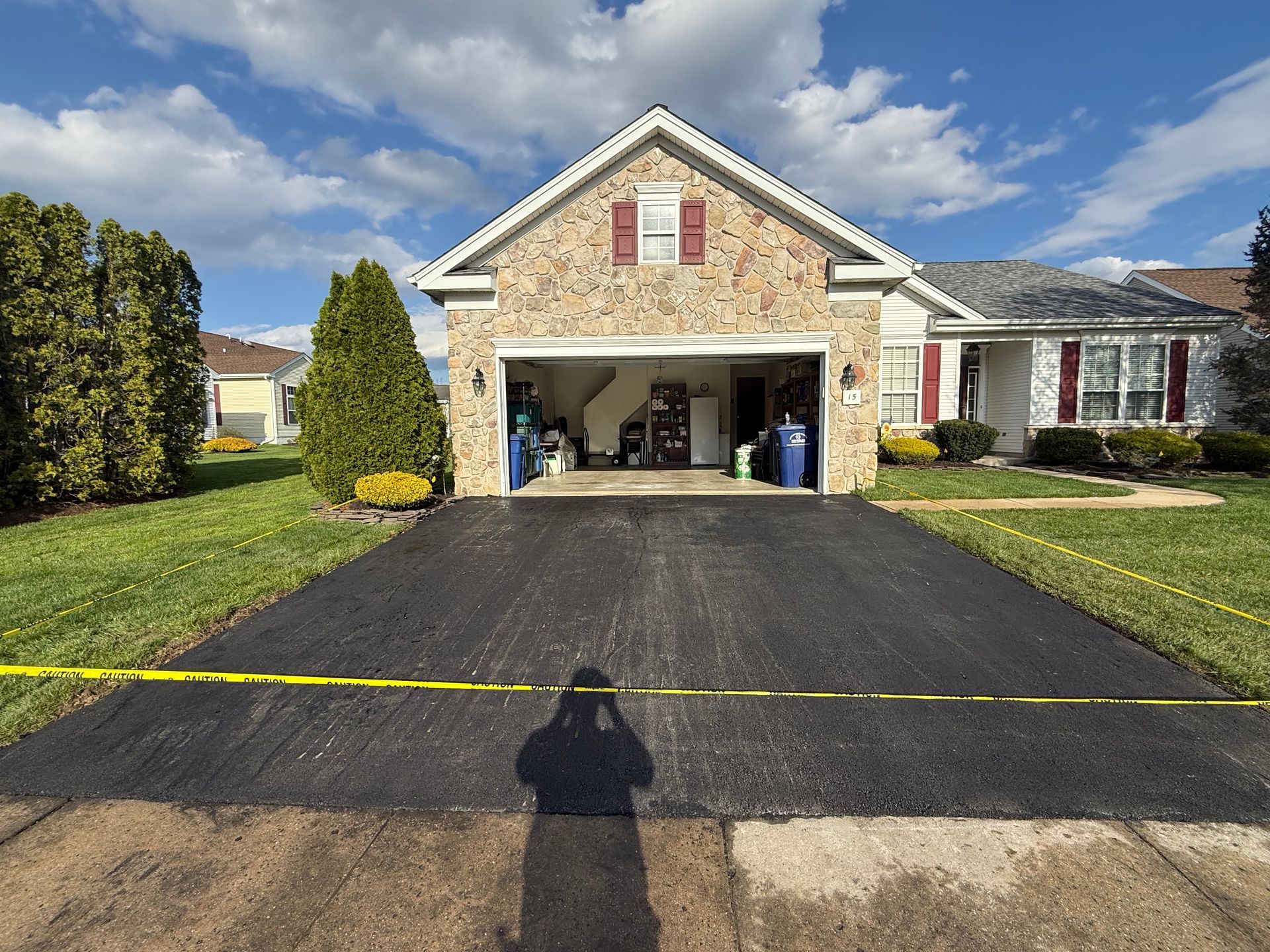 Suburban house with open garage, black driveway, and yellow caution tape across the front