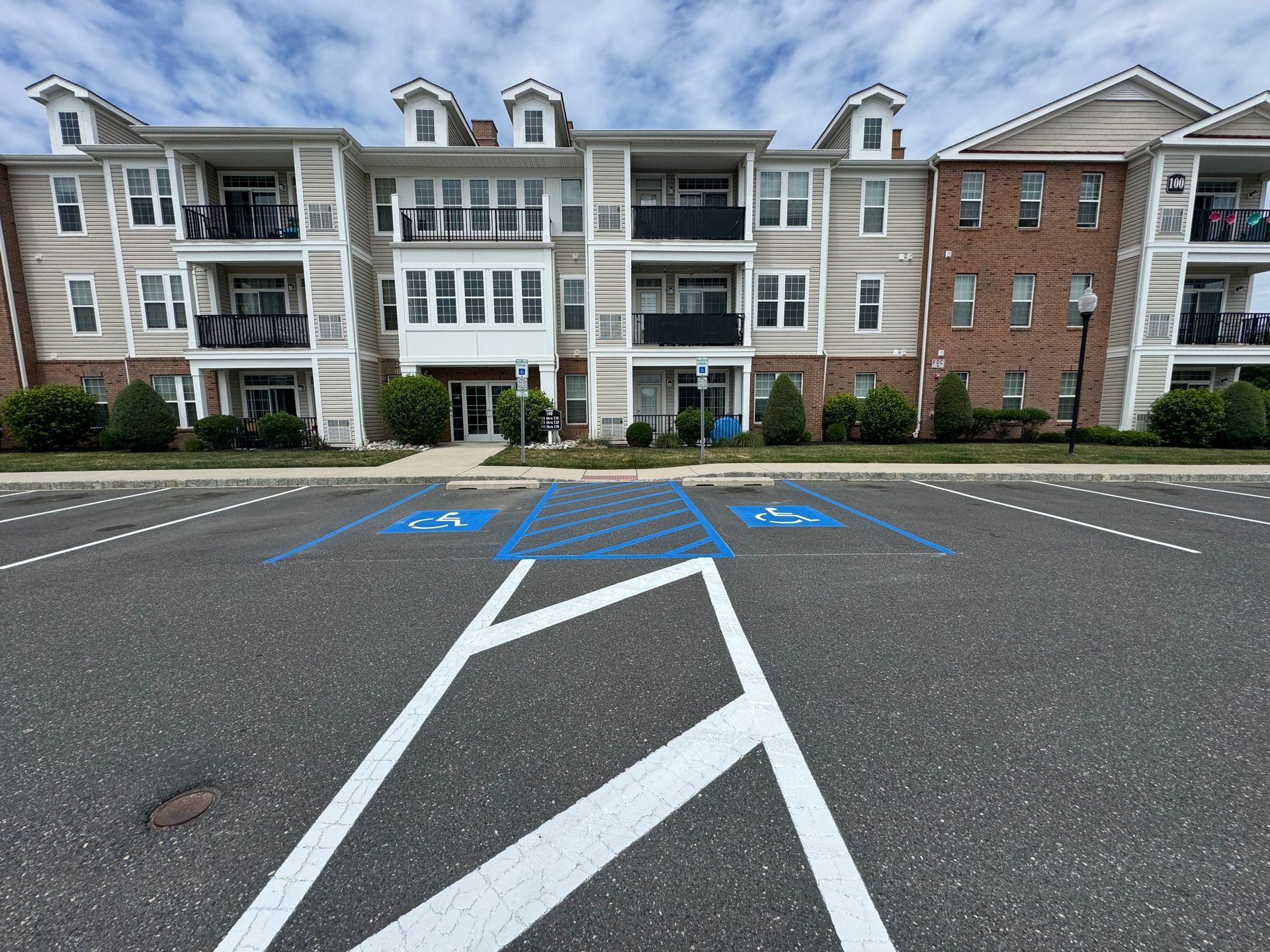 Parking lot with blue handicap parking spaces in front of an apartment building with tan and brick siding.