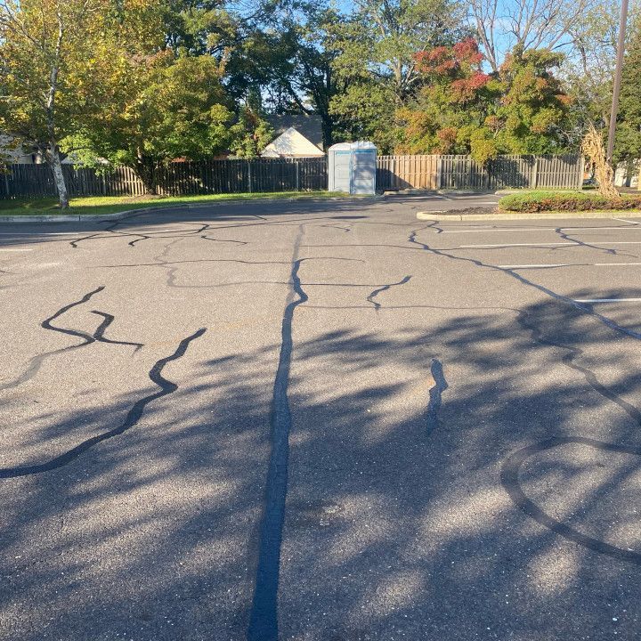 Cracked asphalt parking lot; trees and a portable toilet are in the background.