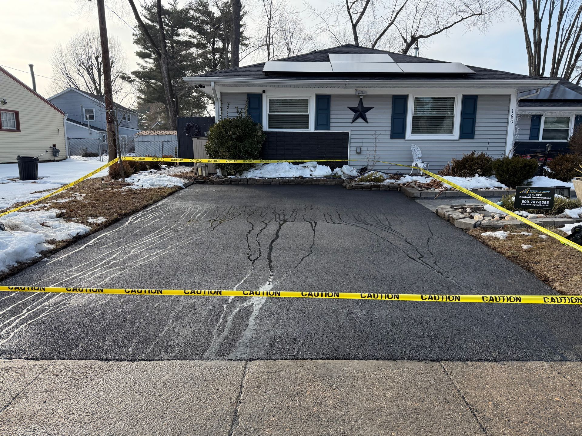 House with blue shutters behind taped-off cracked driveway and snow patches