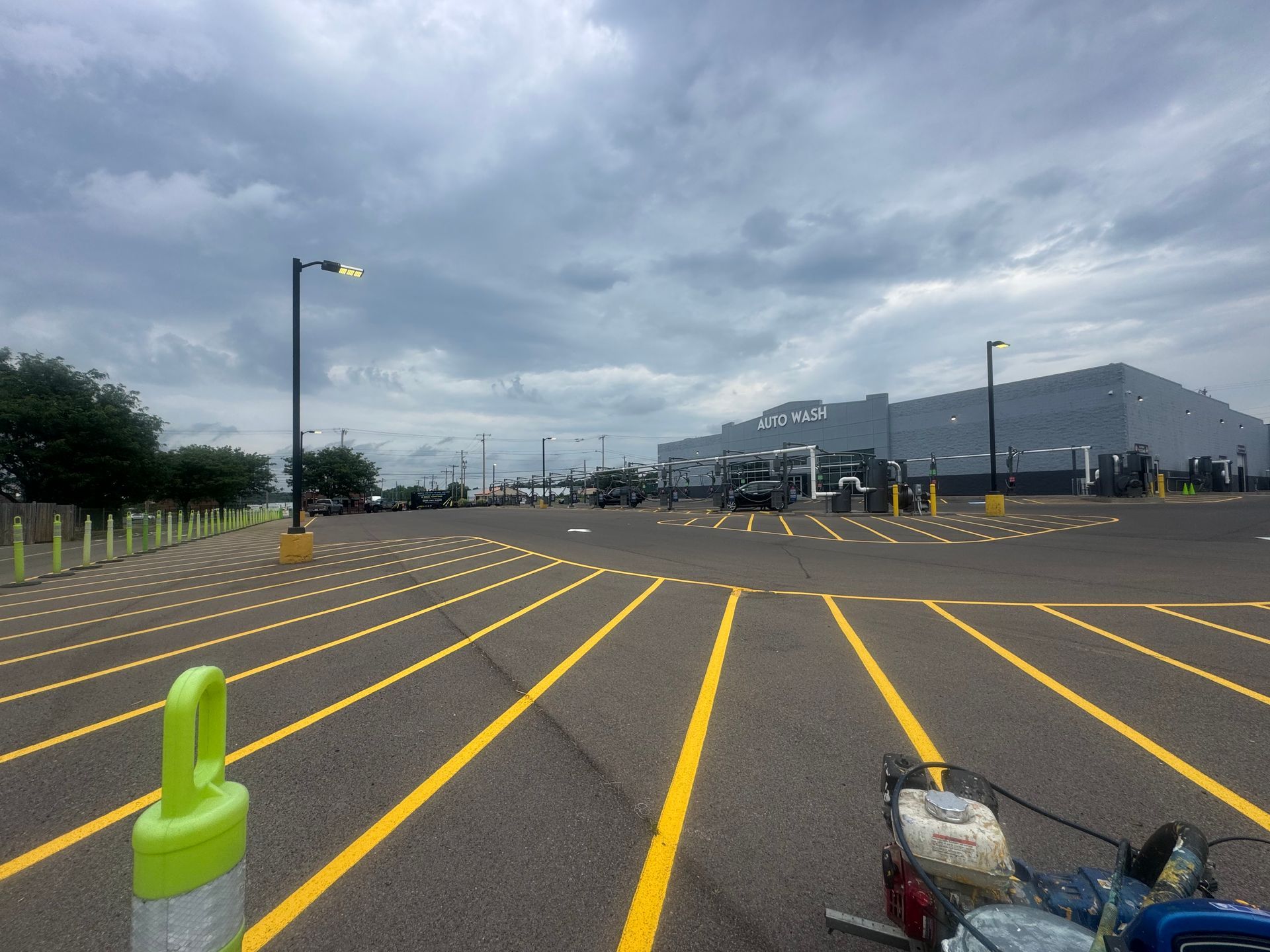 View of newly painted yellow parking space lines in a large lot, with a building in the background. Cloudy sky.