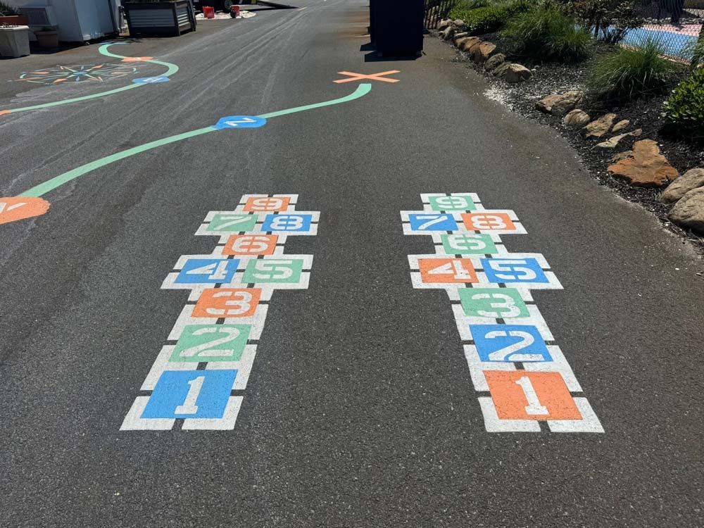 Two hopscotch games painted on asphalt with colorful numbers and a green path.