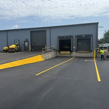 Exterior of a warehouse with loading docks.  Workers are present near fresh asphalt and yellow markings.