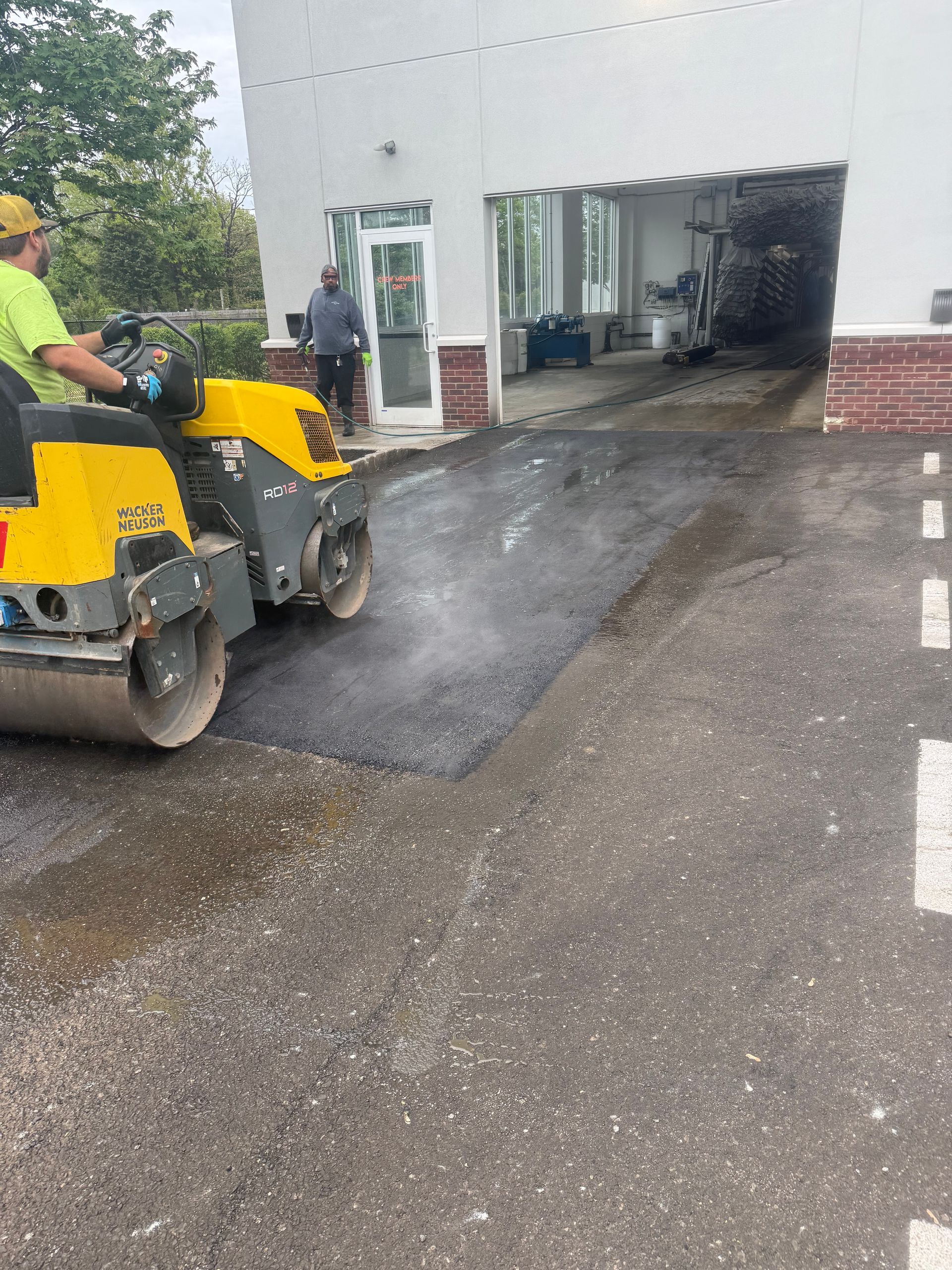 Road workers paving asphalt at a building entrance with a yellow roller machine