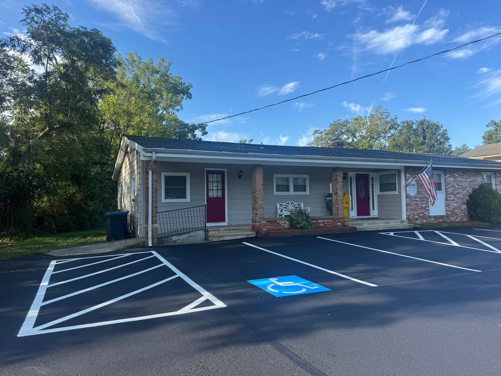 Exterior view of a small building with two units, parking spaces, and a handicap parking spot. Blue sky.