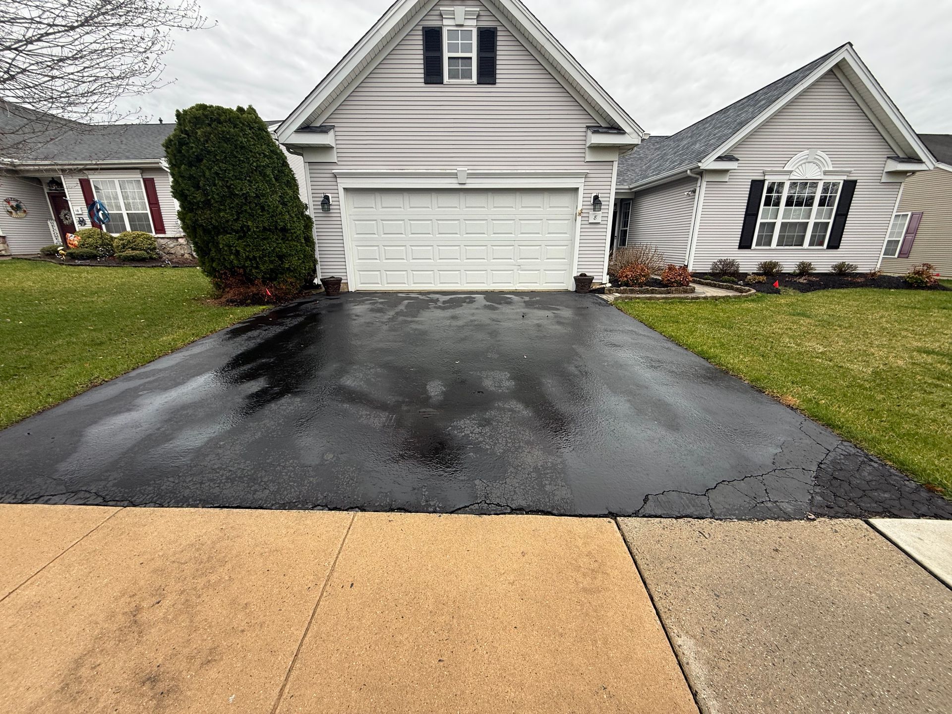 Suburban house with a black driveway and light-colored garage, viewed from the street