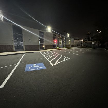 Night exterior of a building with a parking lot. A blue handicap symbol is painted on the asphalt. Lights illuminate the area.