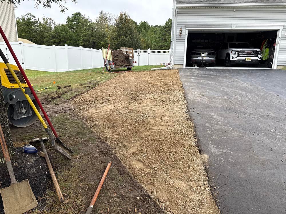 Gravel driveway beside a lawn and white fence, leading to an open garage with two cars inside.