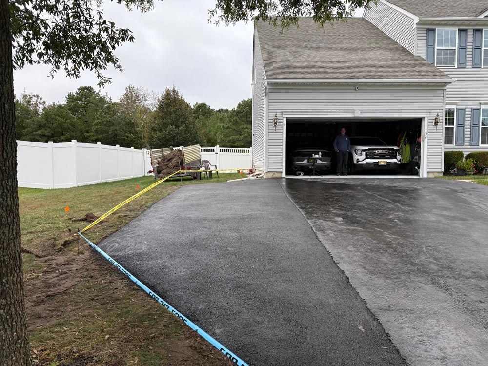 Freshly paved driveway beside a white house with open garage and fenced yard