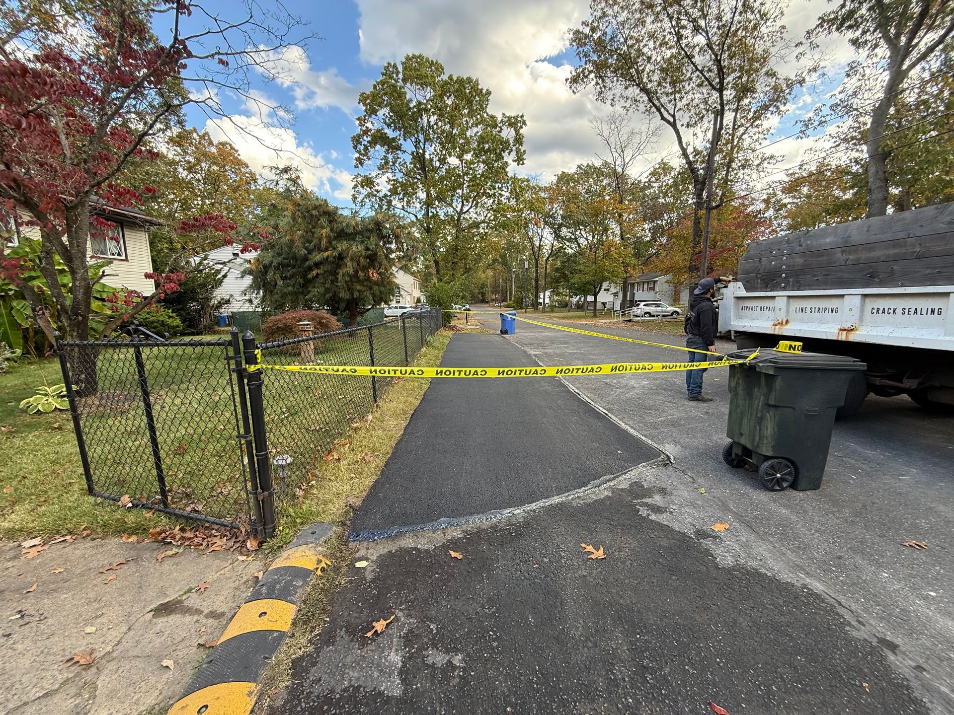 Residential street blocked by yellow caution tape, with trash bins and a parked truck on the right.