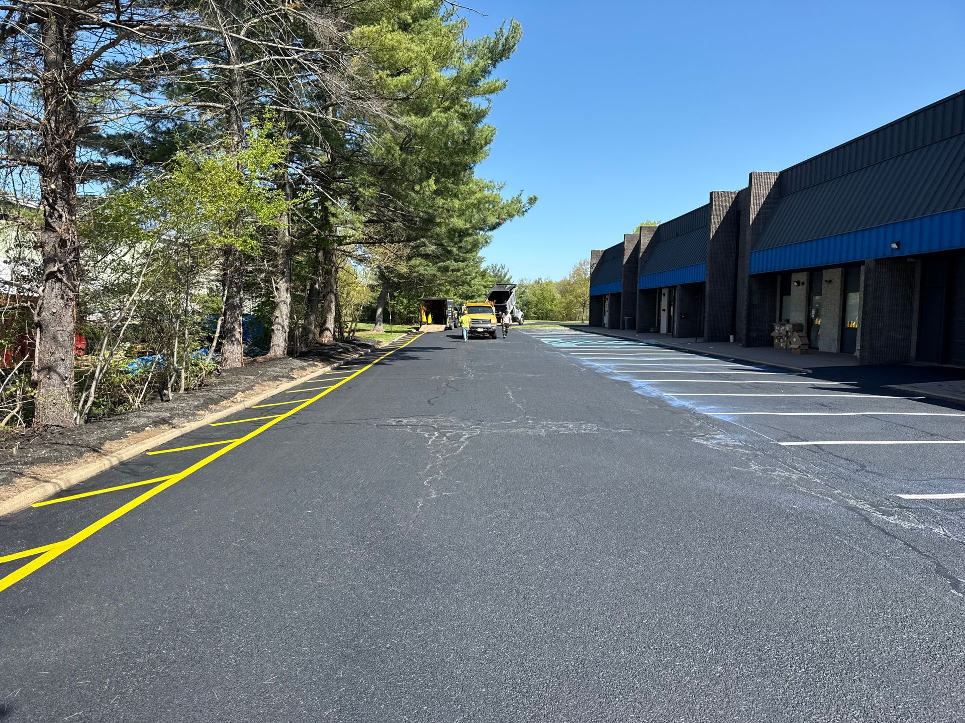 Empty parking lot beside a blue-roofed building and trees on a sunny day