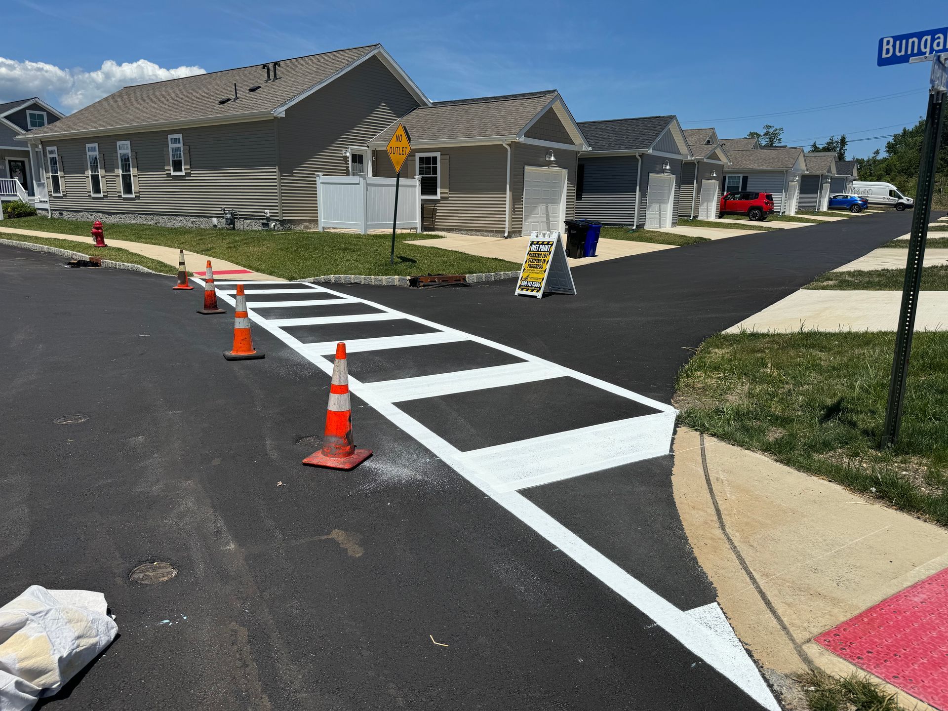 Newly painted crosswalk at a street corner with orange traffic cones and houses in the background.