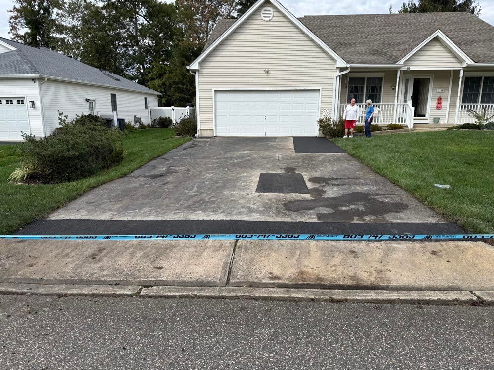 Driveway and garage of a beige house with people standing on the front porch.