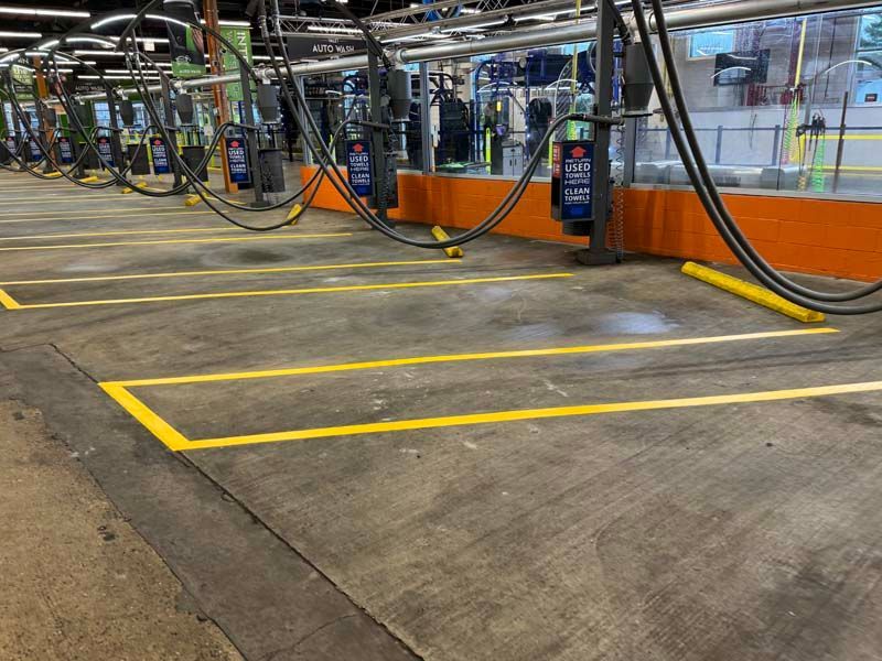 Empty car wash bays with yellow painted lines and overhead equipment. Concrete floor.