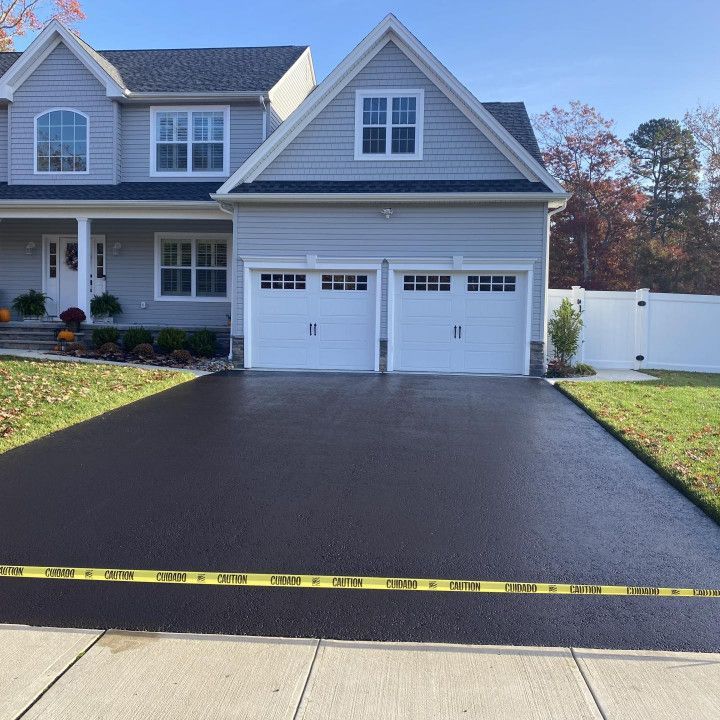 Newly paved asphalt driveway in front of a light gray house with a two-car garage.