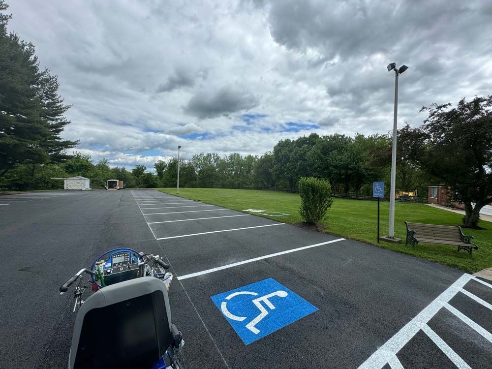 Wheelchair in parking lot with accessible parking space, grassy area, and cloudy sky.