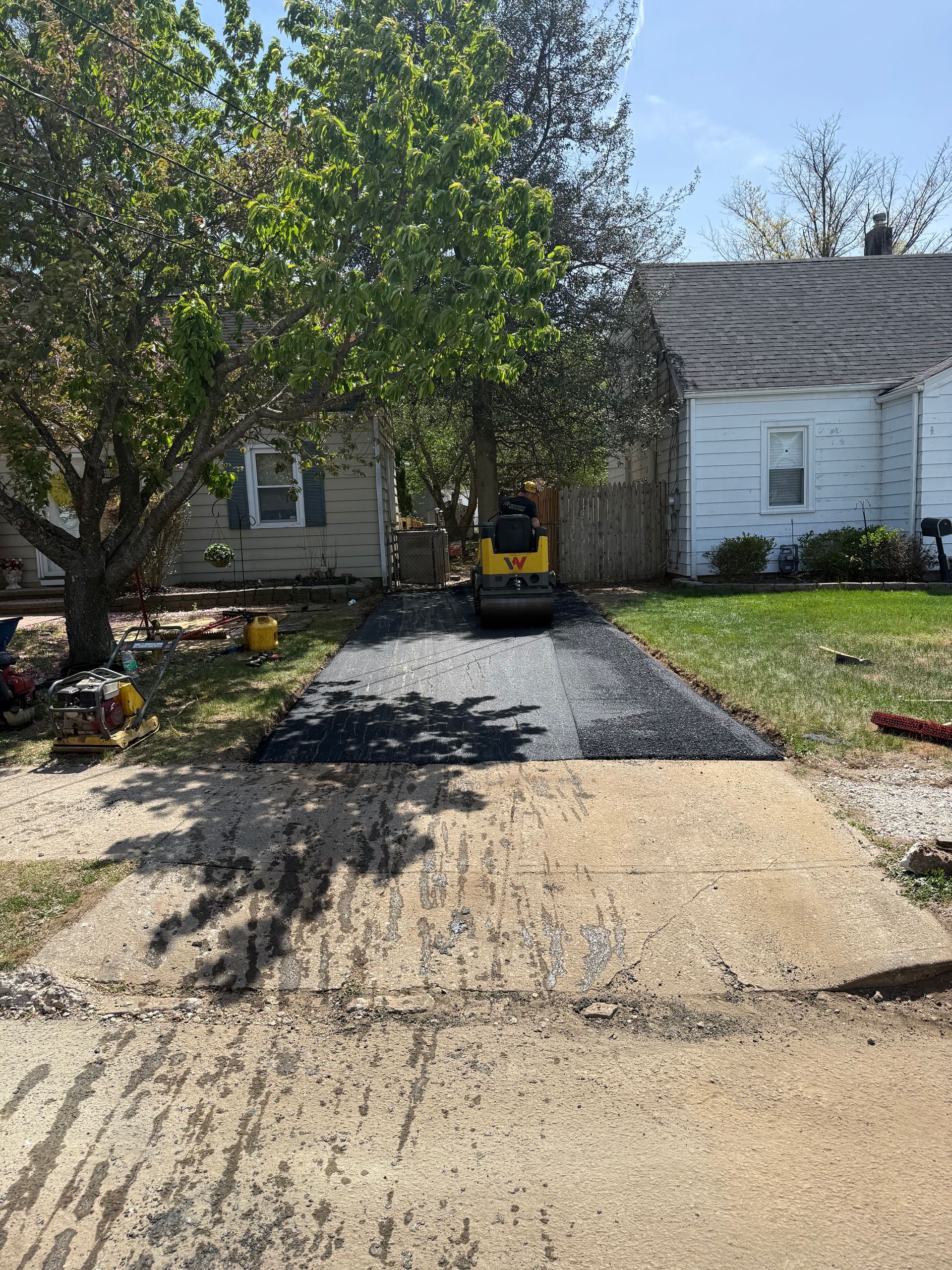 Suburban driveway with gravel, trees, and a yellow utility vehicle parked in front of a house.
