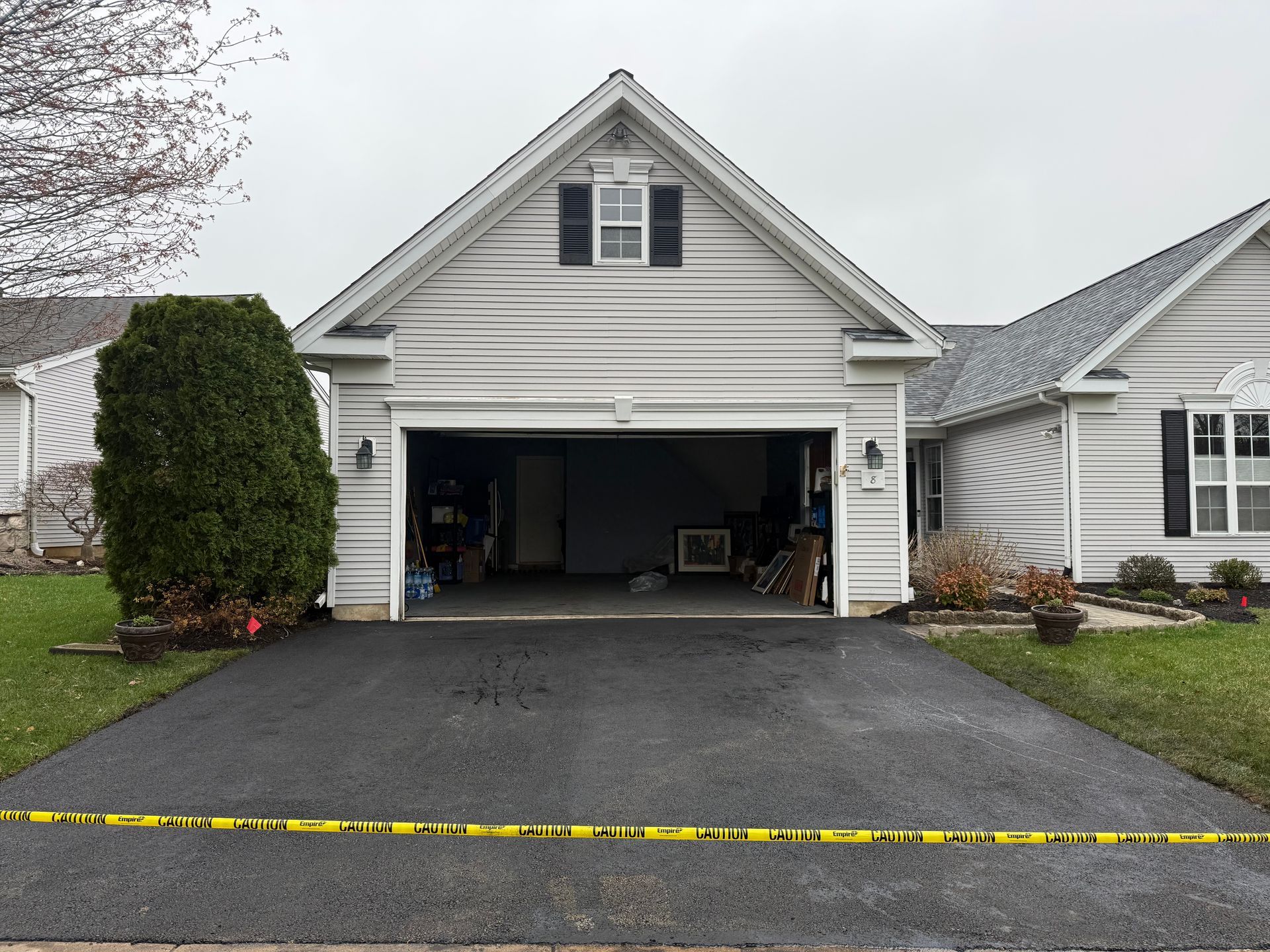Suburban house with open garage and newly paved driveway, marked by yellow caution tape.