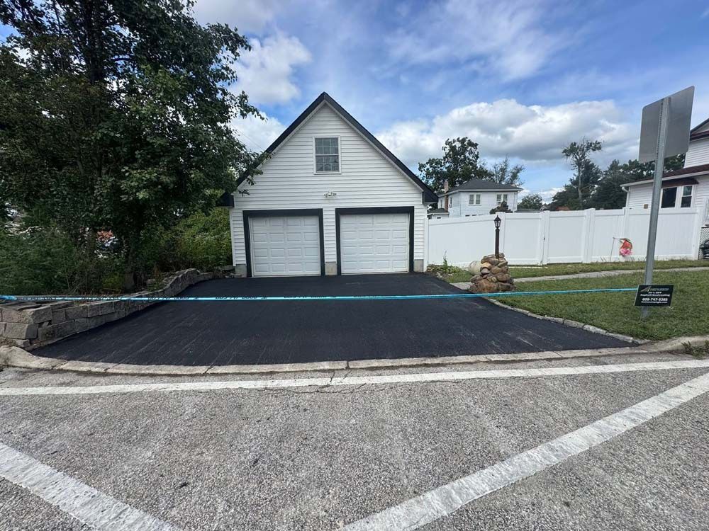 White detached garage with two doors, black driveway, and a small front lawn under a cloudy sky.