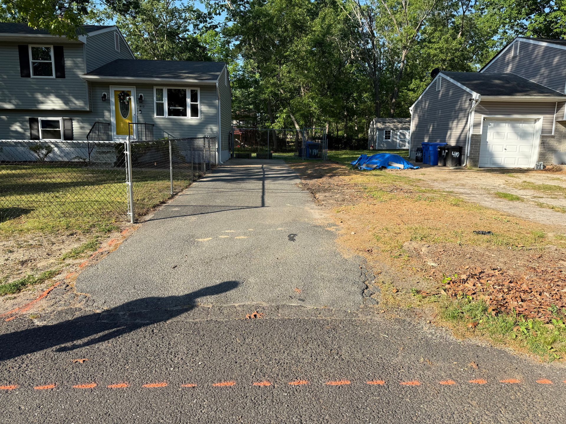 Gravel driveway between two houses, with a chain-link gate and a garage on the right.