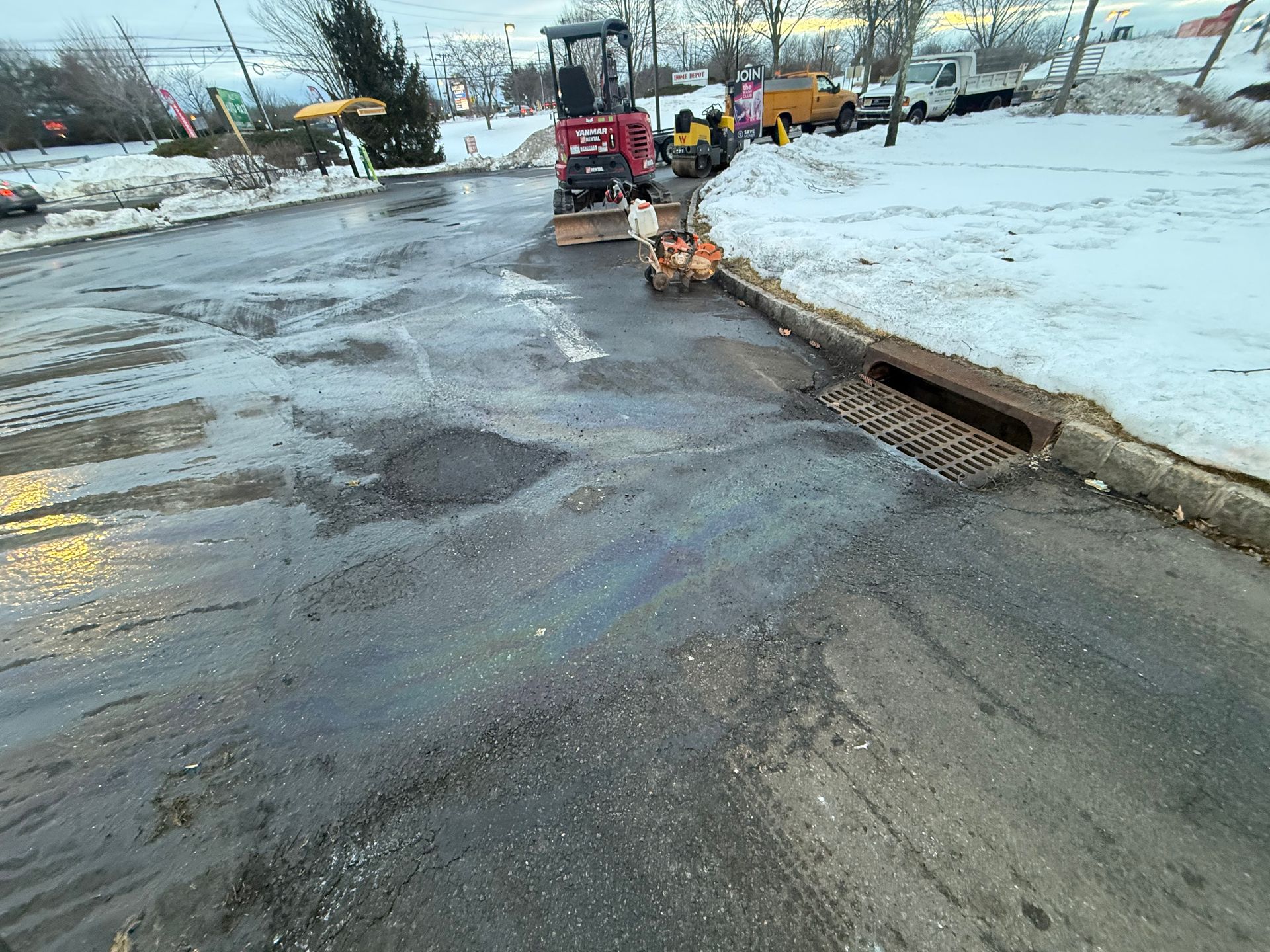 Road crew clearing snow and ice from a wet, slushy street near a storm drain