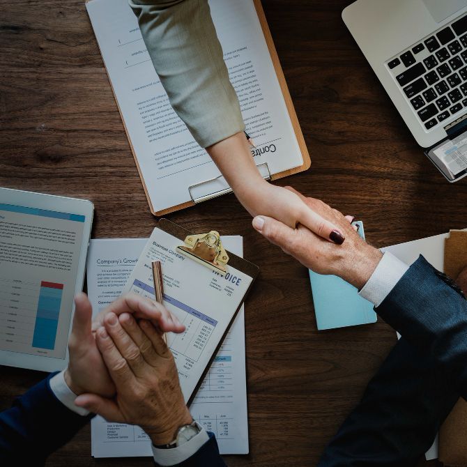 A man and a woman shaking hands over a table with papers and a laptop  for Fraser Corporate Finance.