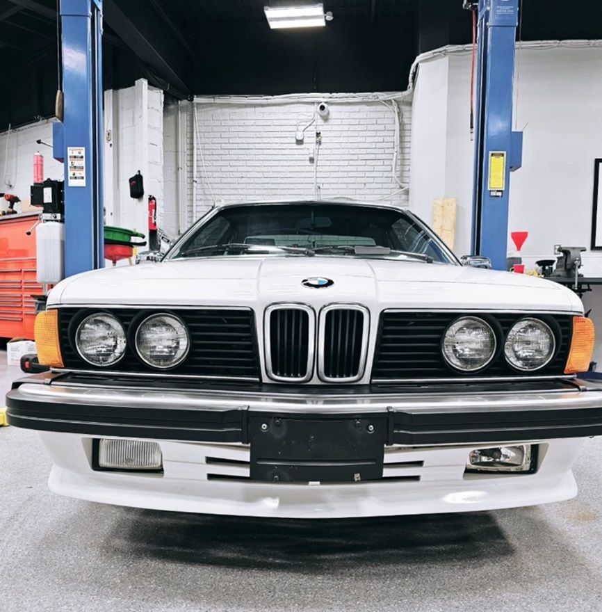 Front view of a white BMW in a garage with blue vehicle lifts