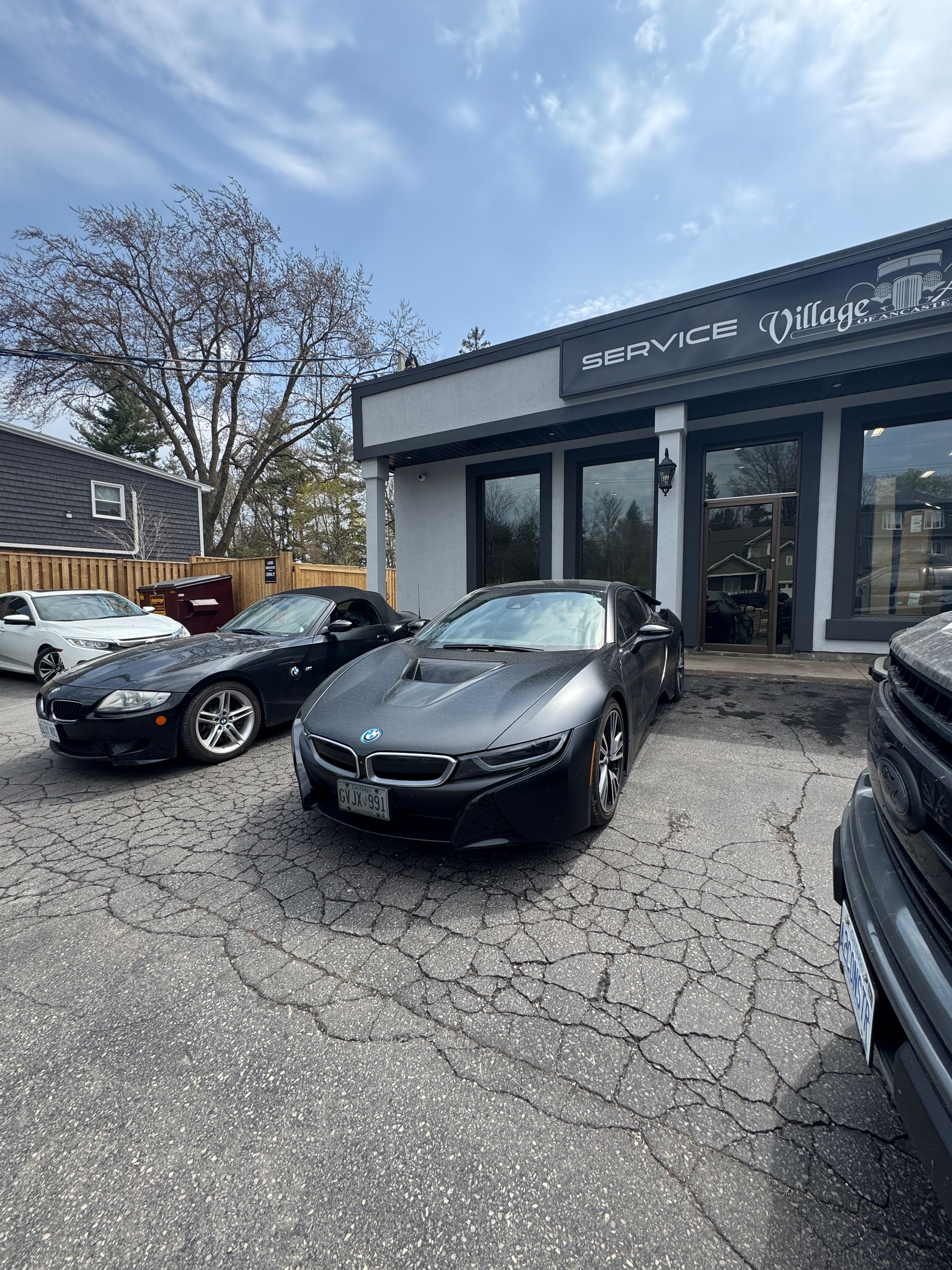 Black sedan parked outside a service shop with several cars in a cracked asphalt lot