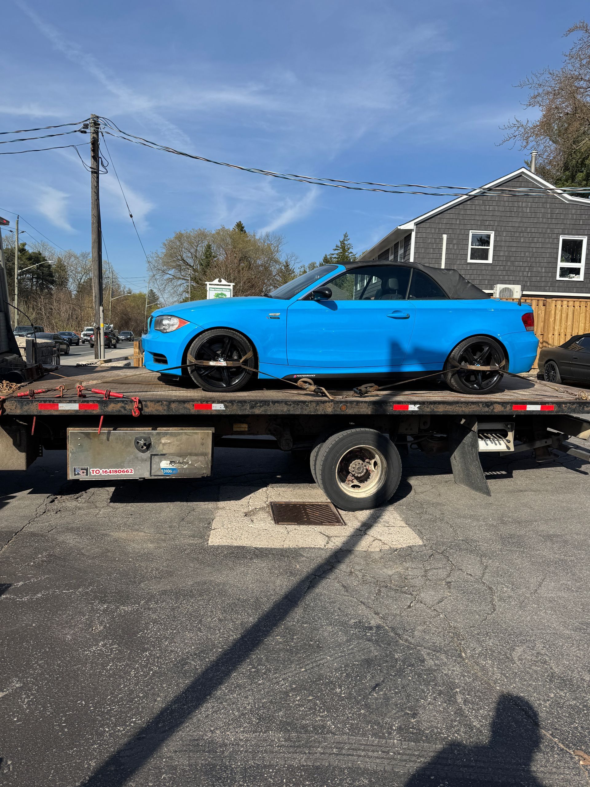 Bright blue sports car on a flatbed tow truck in a sunny parking lot