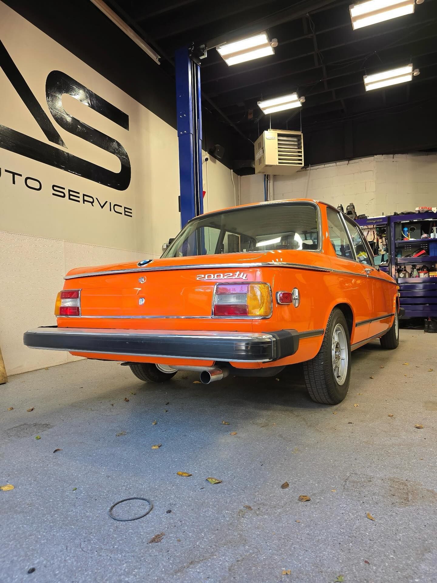 Orange classic car in an auto shop garage, viewed from the front-left angle.