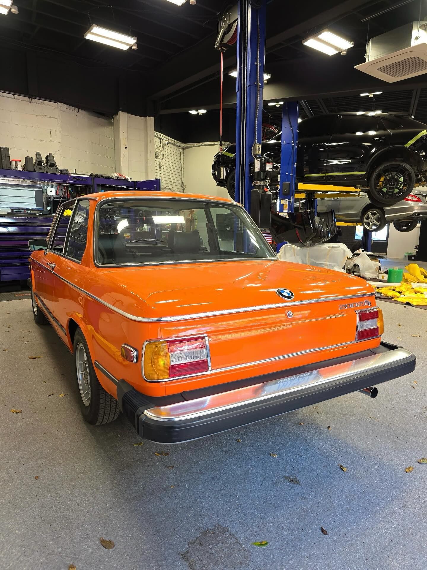 Orange vintage BMW sedan in a car workshop, seen from the rear on a lift