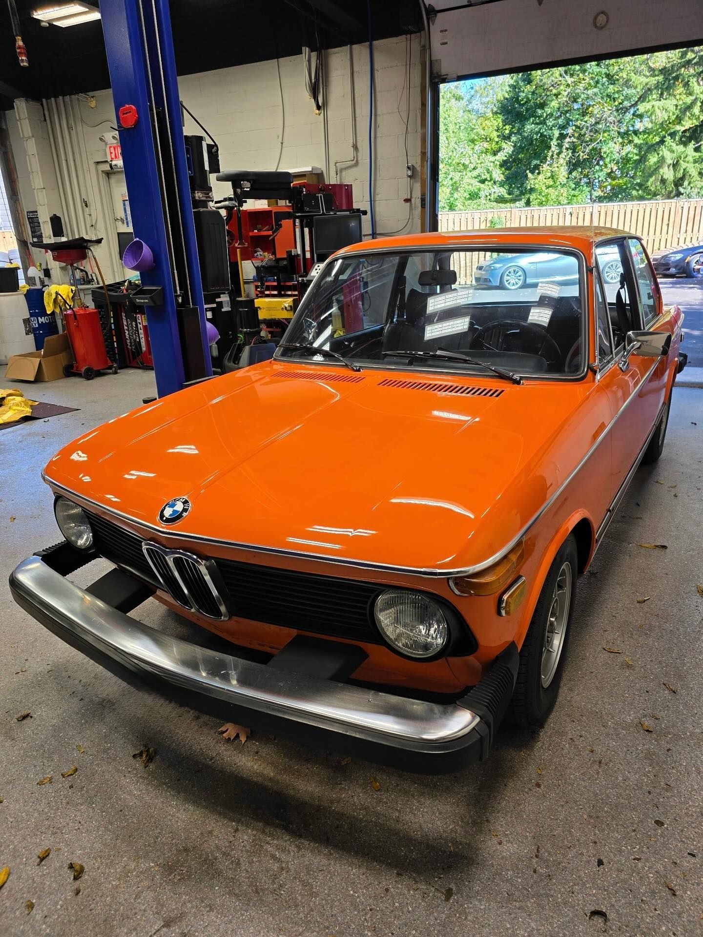 Orange vintage BMW sports car in an auto shop with the hood open and a front bumper guard.