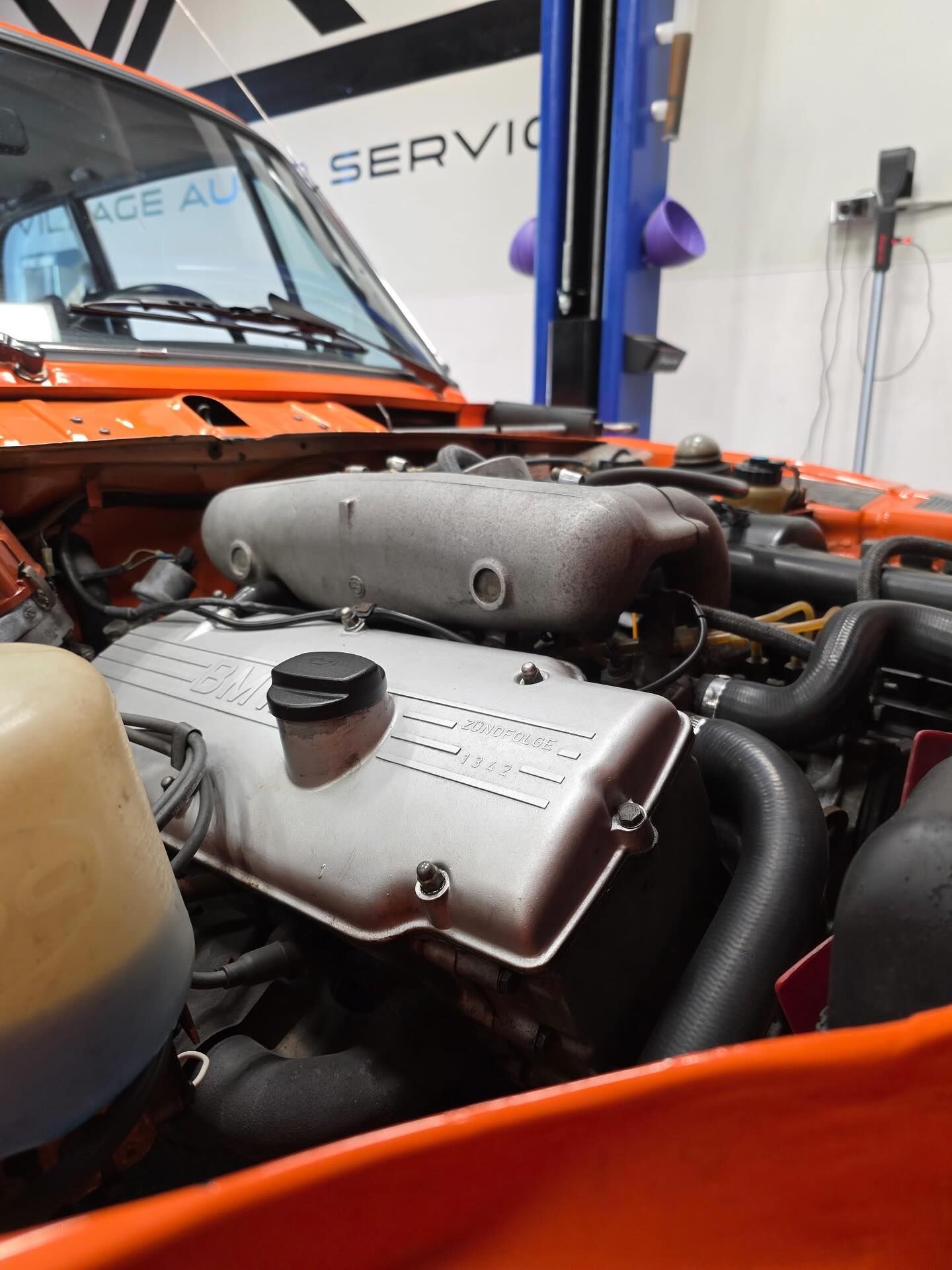 Orange sports car engine bay with exposed mechanical components in a workshop
