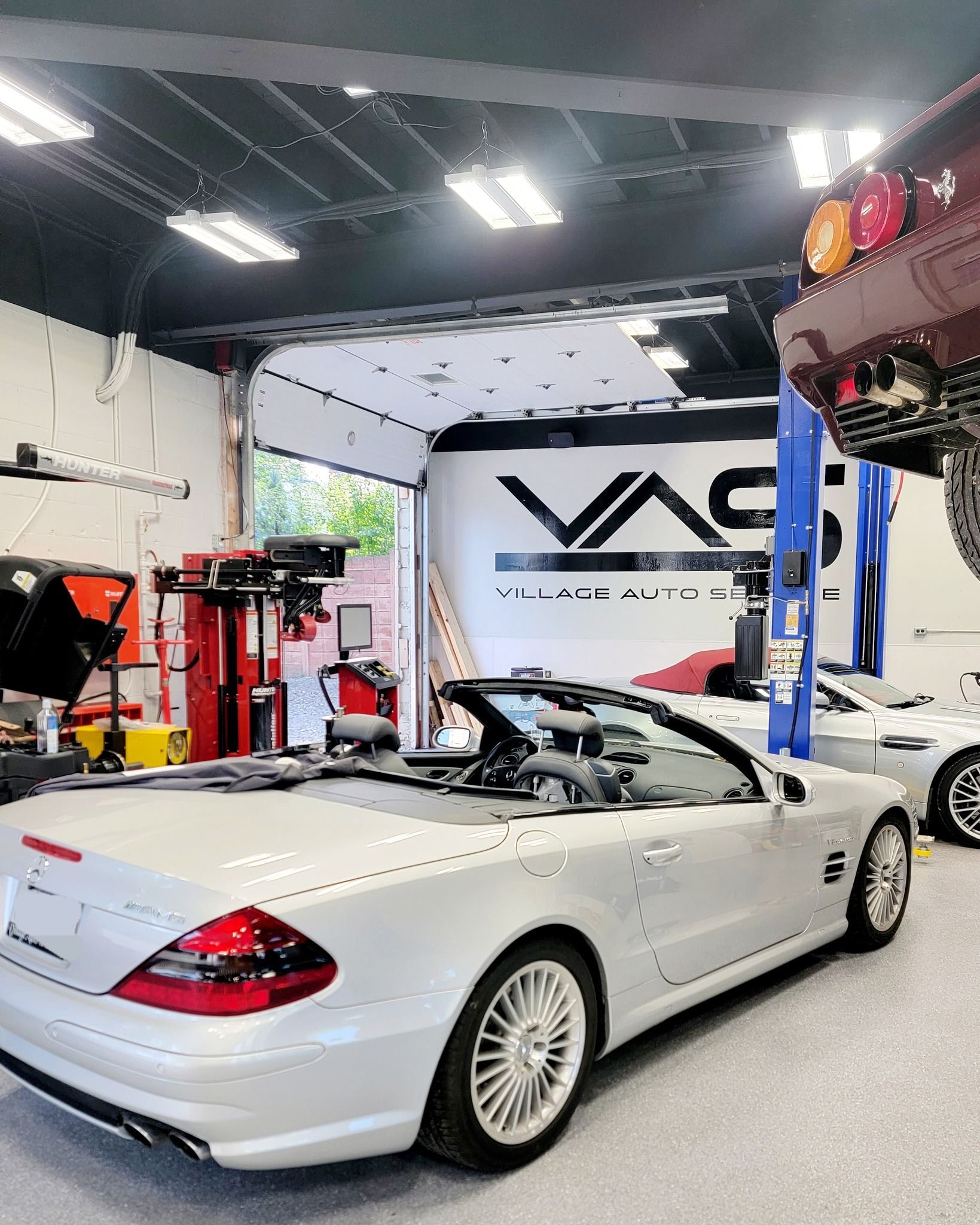 White convertible sports car in an auto shop garage with lifts and equipment, viewed from the rear side.