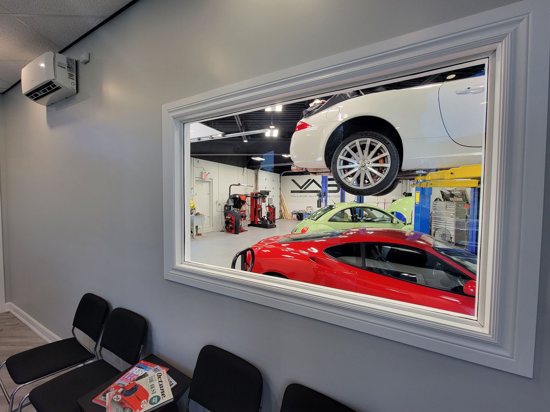 Waiting room with chairs overlooking an auto shop where cars are lifted on service racks.
