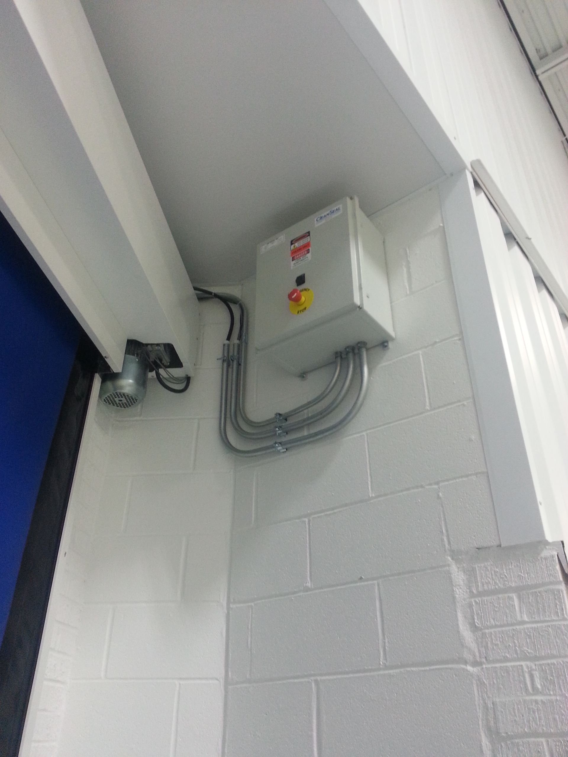 A white box with a yellow sticker on it is hanging on a brick wall.