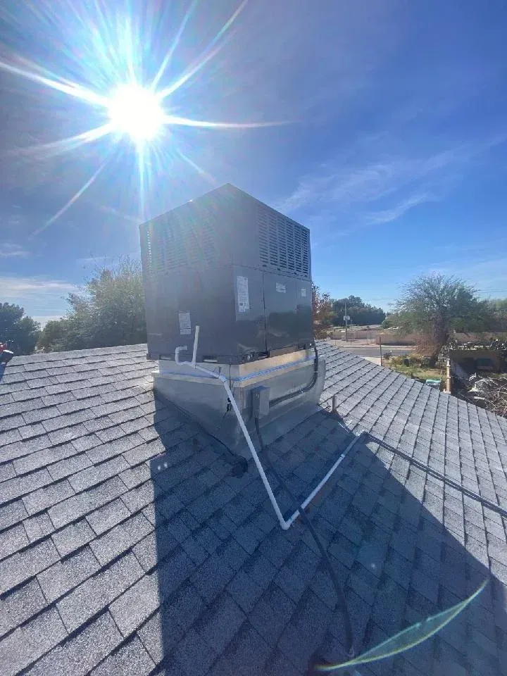 Rooftop HVAC unit on a shingled roof under bright sun and blue sky