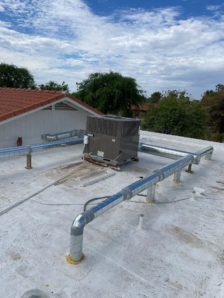Rooftop HVAC unit with metal safety railing on a white roof under a cloudy sky
