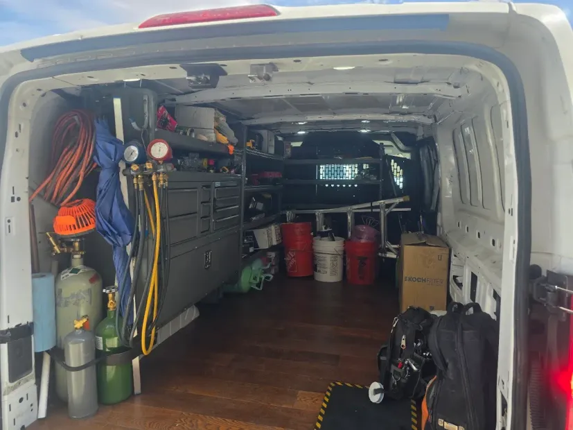 White cargo van interior with organized tools, hoses, gas cylinders, bins, and wooden flooring